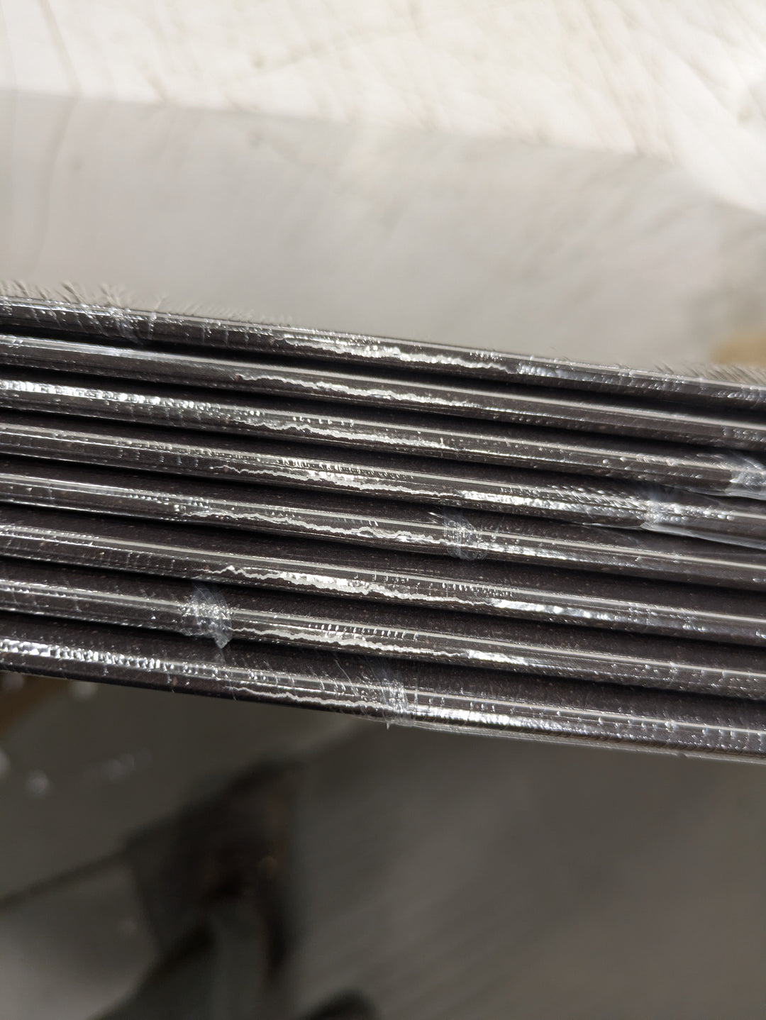 Close-up of the edges of stacked HolyName black boards, layered like limited edition vinyl, with visible white marks or scratches on their surfaces.
