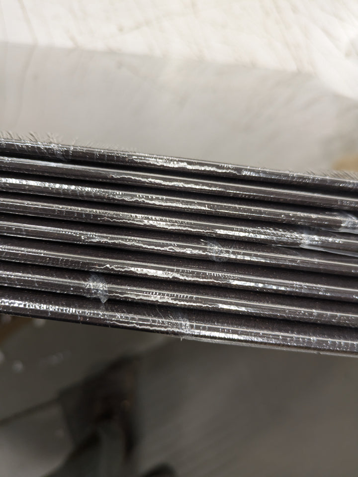 Close-up of the edges of stacked HolyName black boards, layered like limited edition vinyl, with visible white marks or scratches on their surfaces.