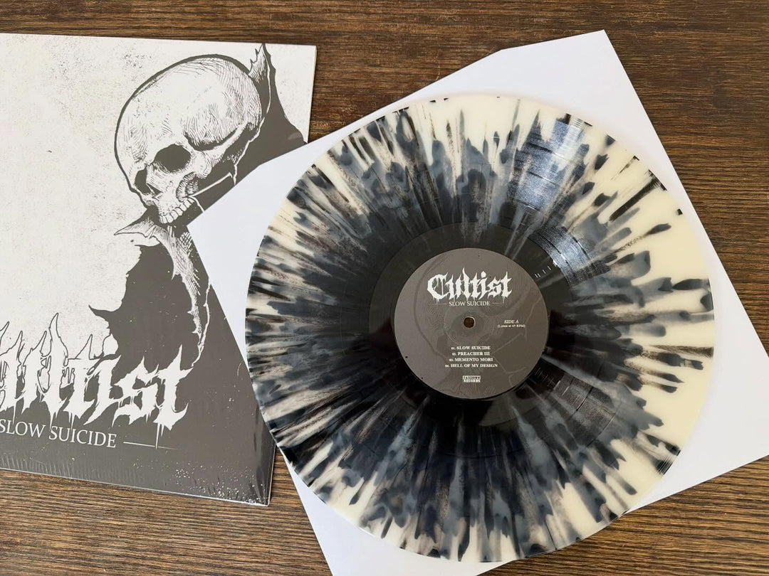 A limited edition Cultist Achromatic Splatter Vinyl LP rests partly on its skull-illustrated Slow Suicide album cover, with a digital download card beside it on a wooden surface.