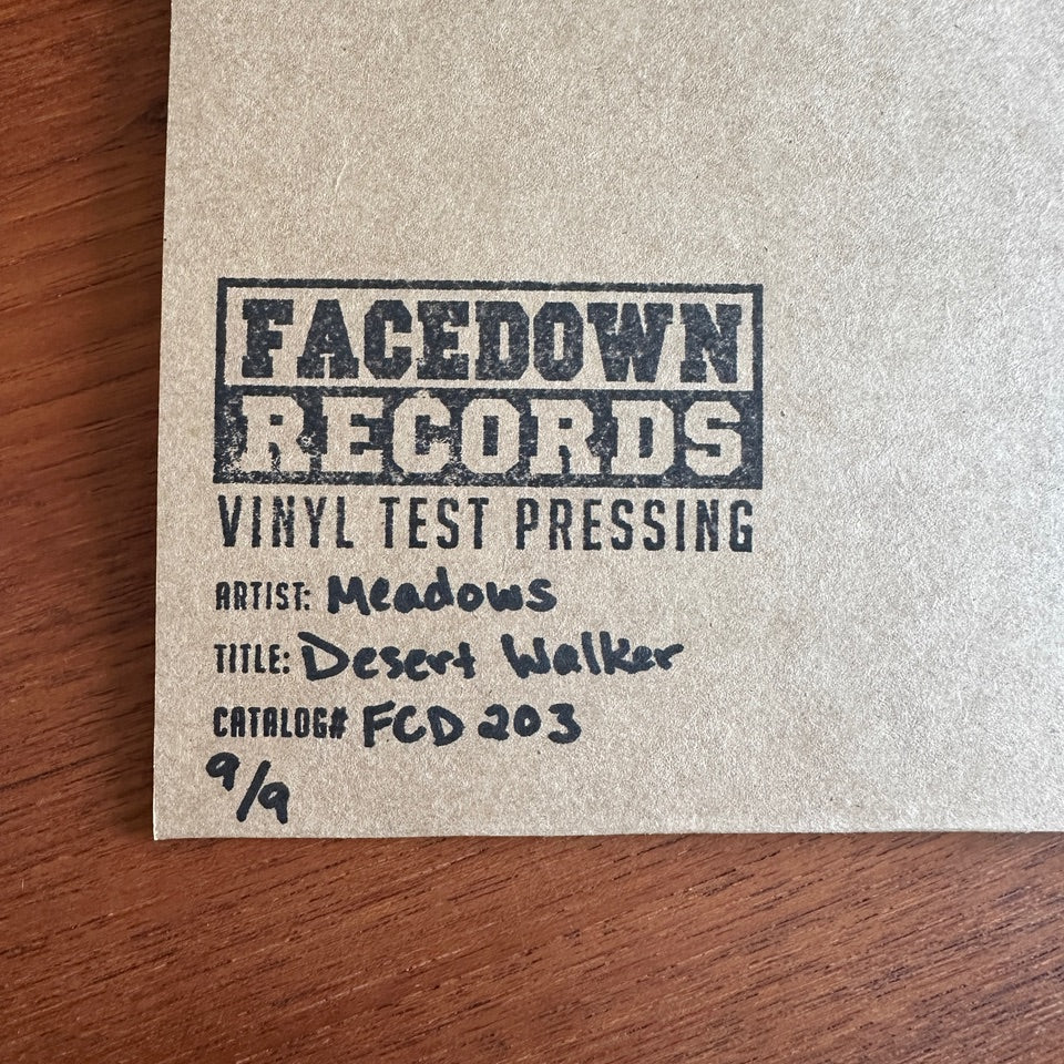 A tan record sleeve stamped with Facedown Records Vinyl Test Pressing rests on a wooden surface. Handwritten text reads: Artist: Meadows, Title: Desert Walker LP, Catalog#: FCD 203, 9/9—marking this as an exclusive Test Pressing.