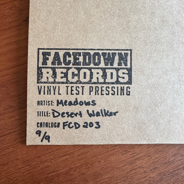 A tan record sleeve stamped with Facedown Records Vinyl Test Pressing rests on a wooden surface. Handwritten text reads: Artist: Meadows, Title: Desert Walker LP, Catalog#: FCD 203, 9/9—marking this as an exclusive Test Pressing.