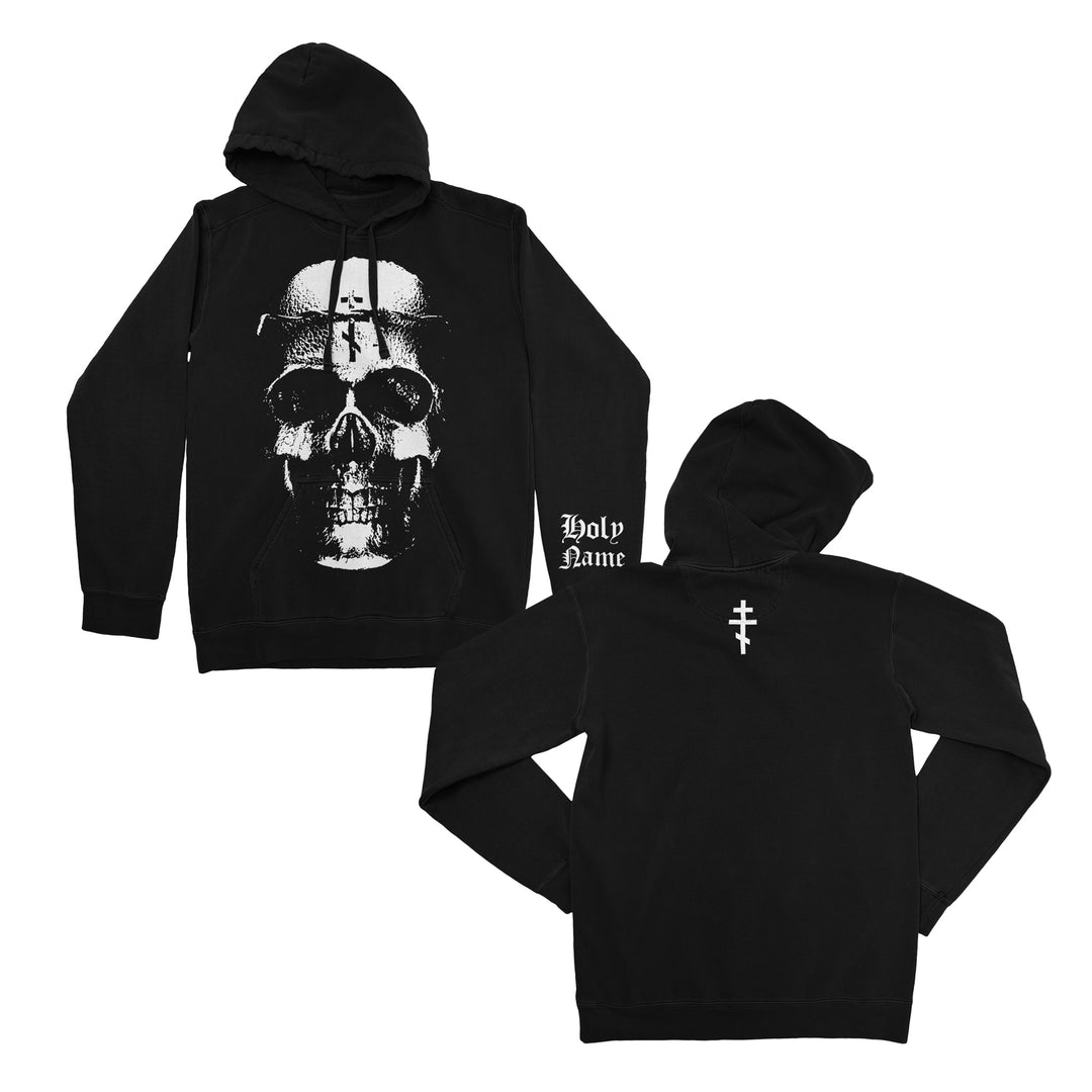 Black hoodie with a large white skull graphic on the front, Holy Name text on one sleeve, and a white cross-like symbol on the back near the hood. Crafted from soft ring-spun cotton fleece, this classic fit hoodie by Independent Trading Company offers both comfort and bold style. Both front and back views are shown.