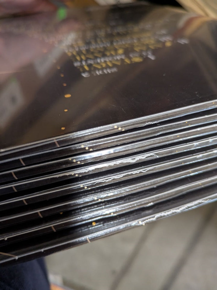 A stack of black and white rectangular objects, including Confessions Of A Traitor's limited edition Golden Eclipse vinyl, neatly arranged with split seams visible along the edges.