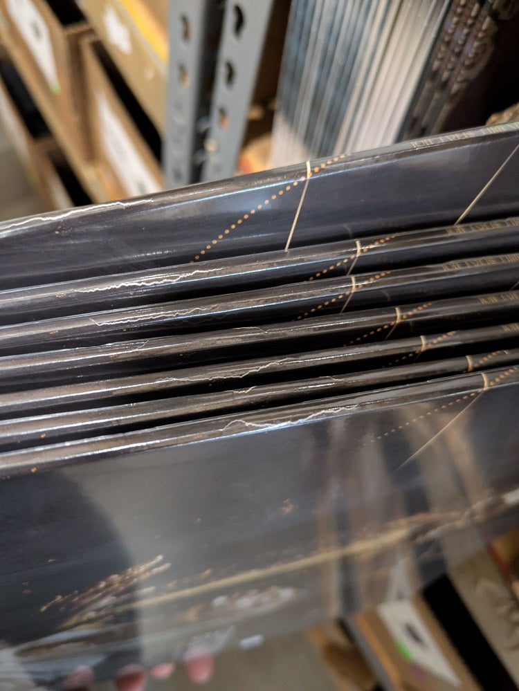 Close-up of a stack of Confessions Of A Traitor limited edition Golden Eclipse vinyl sleeves with split seams along the top edges, displayed on a metal shelf in a storage or retail setting.